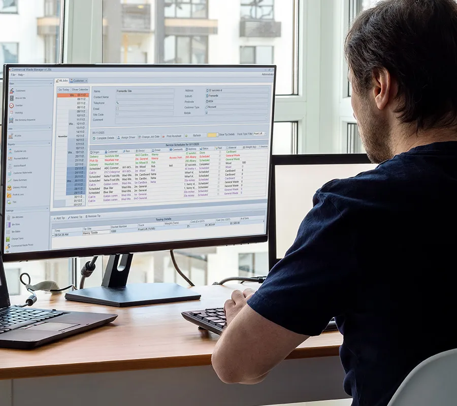 Office worker using CommercialWasteManager on a desktop monitor to manage commercial waste pickups and billing.
