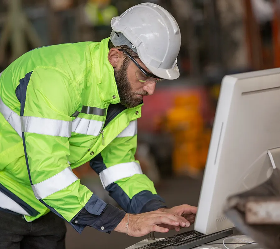 Worker in high-vis and hard hat using ScrapManager scrap metal tracking software at a scrap facility.